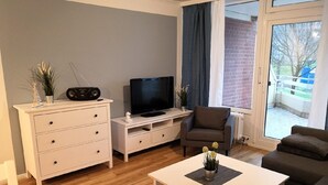 A modern living room with a white entertainment unit, a flat-screen TV, a brown armchair, and a white coffee table. - Haus Belvedere App. 7 Inkl. Wlan (Grömitz)