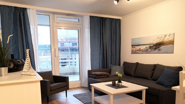 A modern living room with a sofa, coffee table, and a view through a glass door. - Haus Belvedere App. 7 Inkl. Wlan (Grömitz)