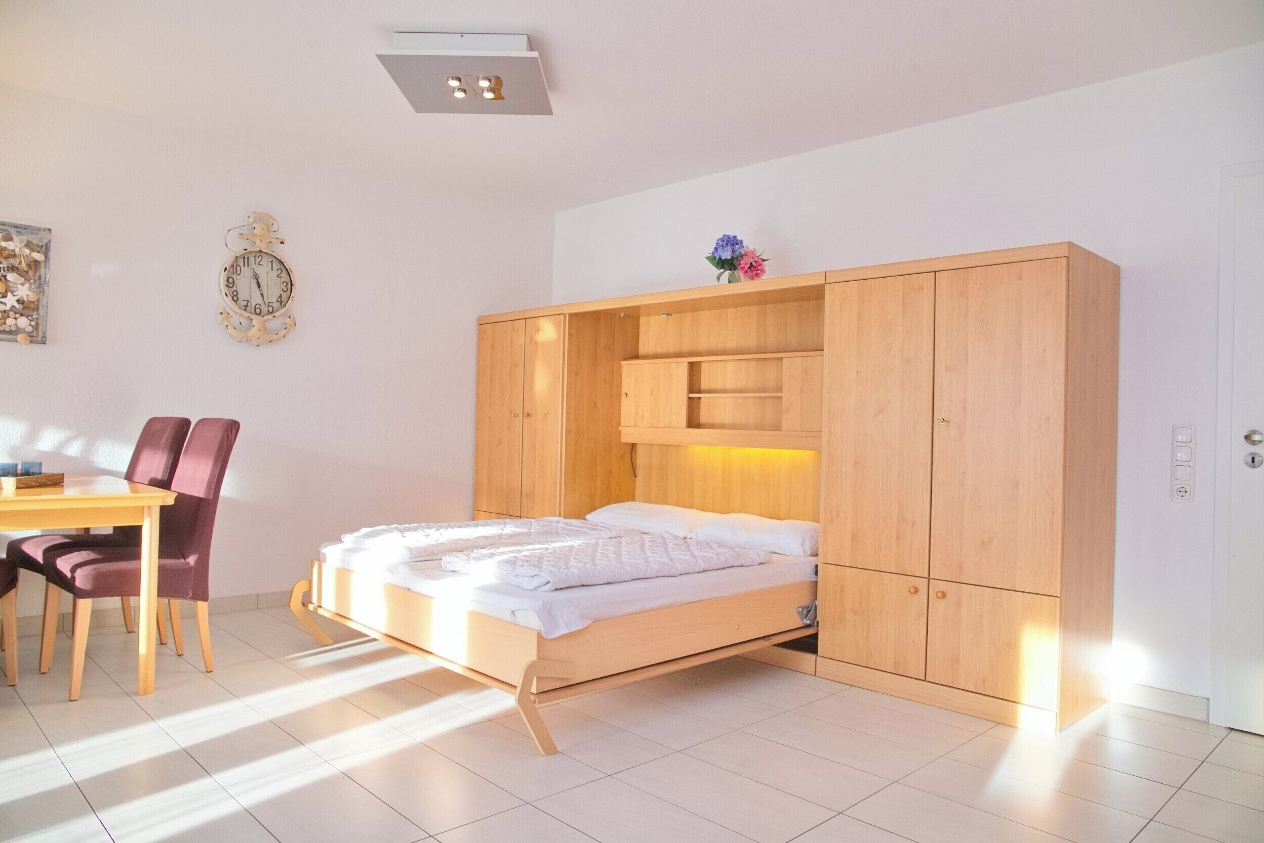 Een kleine slaapkamer met een bed, een houten garderobe, een bureau en een stoel.