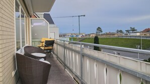 A balcony with wicker chairs and a table, overlooking a construction site and a green area. - Stettiner Str. 55 Inkl. Wlan (Grömitz)