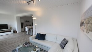 A modern living room with a white sofa, a glass coffee table, and a flat-screen TV. - Stettiner Str. 55 Inkl. Wlan (Grömitz)