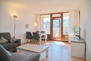A living room with a sofa, coffee table, dining table with chairs, a lamp, and a view through a glass door to the outside. - Haus Belvedere App. 26 Wlan Inkl (Grömitz)