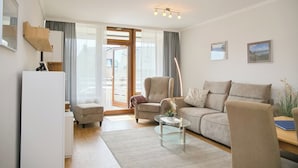 A modern living room with a sofa, armchairs, a coffee table, and a sliding glass door leading to a balcony. - Haus Belvedere App. 28 Inkl. Wlan (Grömitz)