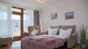 A bedroom with a bed, two armchairs, a small table, and a potted plant. - Haus Belvedere App. 28 Inkl. Wlan (Grömitz)