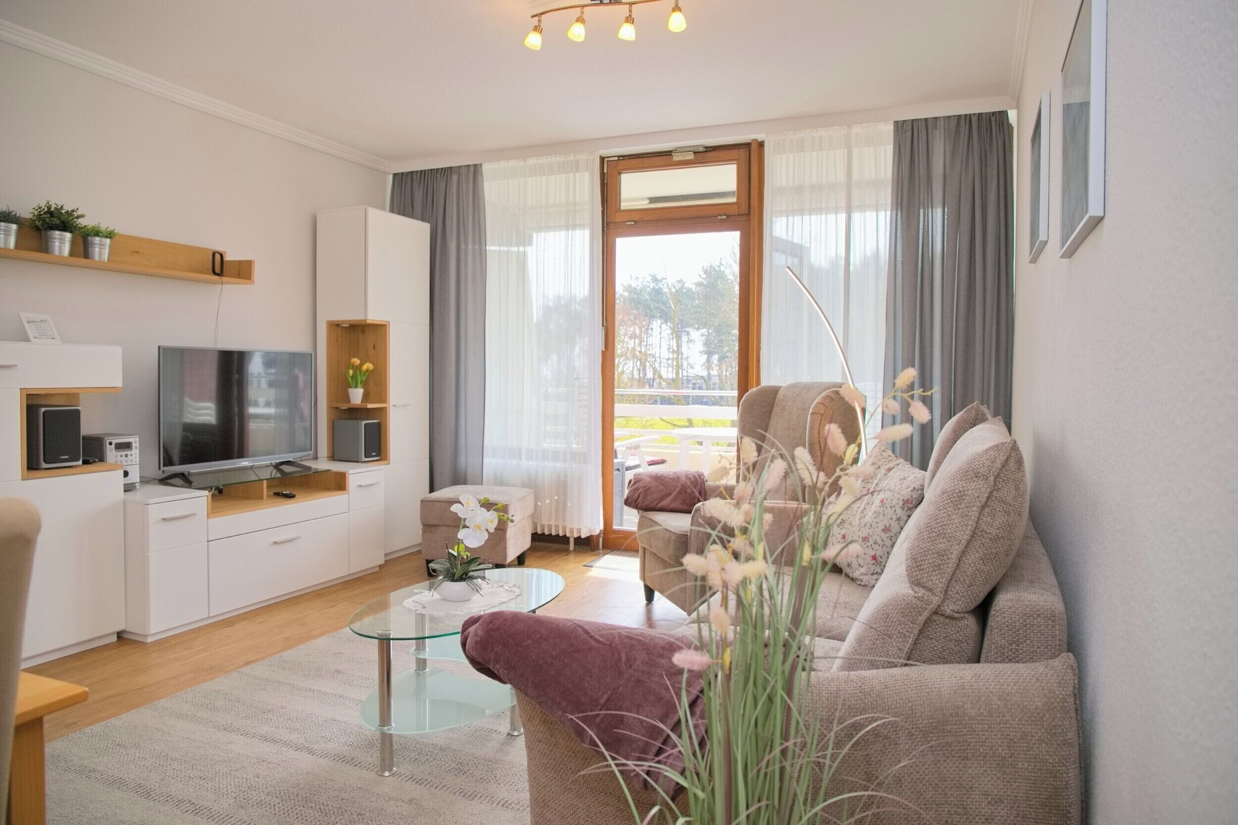 Een moderne woonkamer met een bank, een glazen salontafel, een televisie en een balkon met gordijnen.
