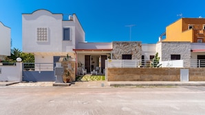 Una casa moderna de dos pisos con fachada de piedra, entrada protegida por una reja y cielo azul despejado.