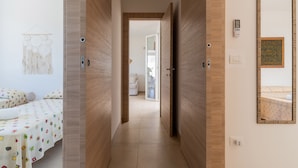 Un pasillo de hotel con puertas de madera, una cama con ropa de cama estampada, un atrapasueños colgado en la pared y un espejo con una obra de arte enmarcada.