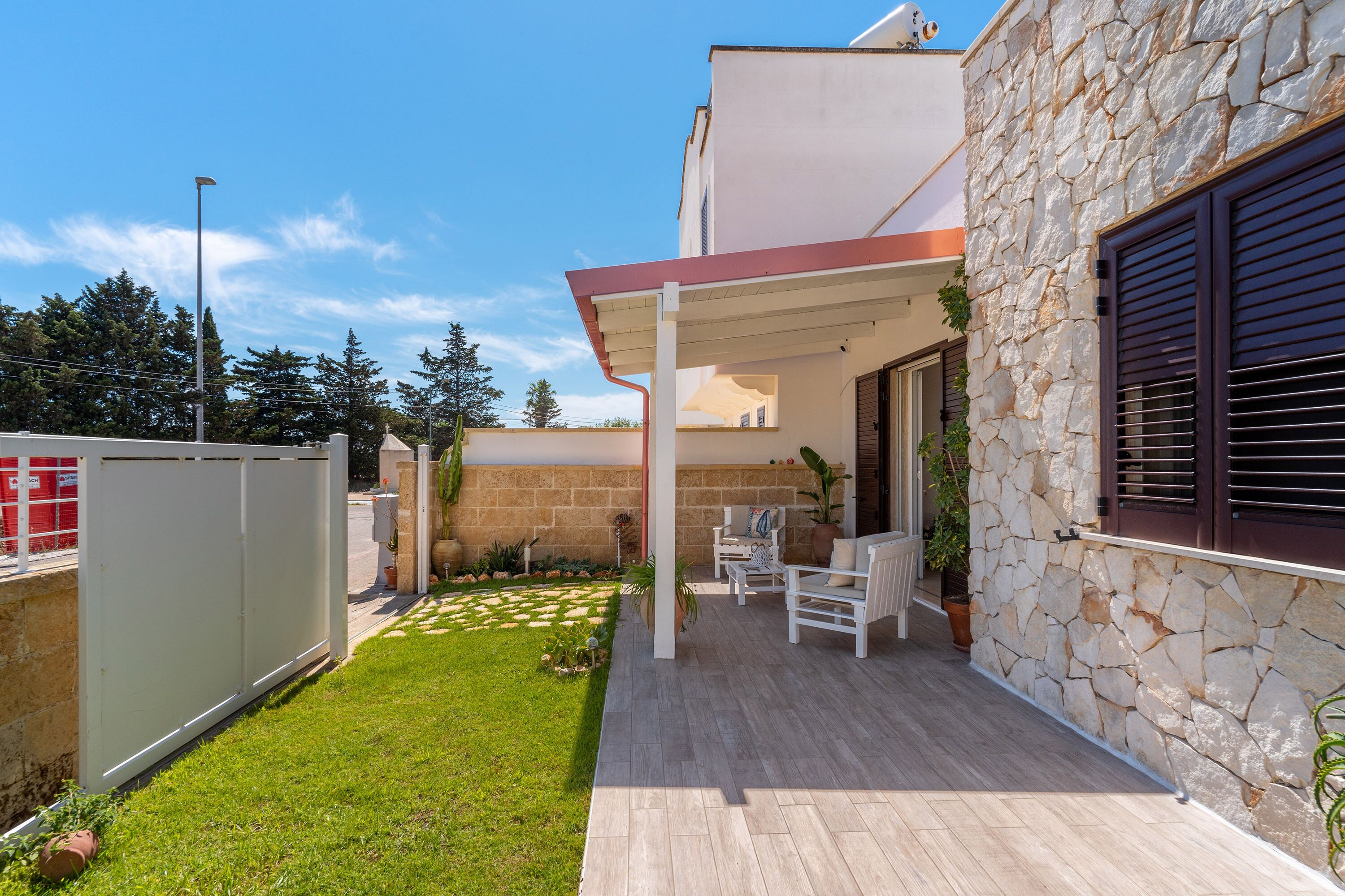Une maison moderne avec une façade en pierre, un patio couvert agrémenté de mobilier d’extérieur et une pelouse bien entretenue.