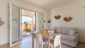 Una sala de estar moderna con un sofá, una mesa de comedor con sillas y un ventanal que da a un espacio al aire libre.
