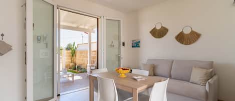 Una sala de estar moderna con un sofá, una mesa de comedor con sillas y un ventanal que da a un espacio al aire libre.