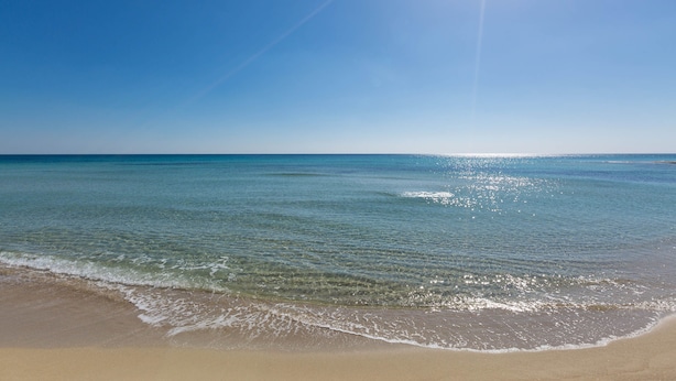 Una playa con agua cristalina y una orilla arenosa bajo un sol radiante.