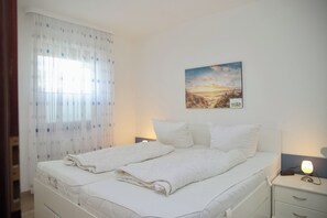 A neatly made bed with white linens, a bedside lamp, and a painting on the wall. - Haus Belvedere App. 34 Wlan Inkl (Grömitz)