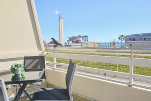 A balcony with a table and chairs, a railing, and a view of a tall building and a body of water. - Haus Belvedere App. 34 Wlan Inkl (Grömitz)