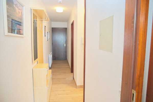 A narrow hallway with wooden flooring, a white wall with a framed picture, and a door at the end. - Haus Belvedere App. 34 Wlan Inkl (Grömitz)