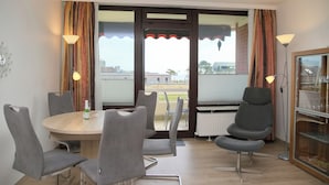 Un coin repas avec une table ronde, six chaises, une bouteille de champagne et une vue dégagée grâce à de grandes fenêtres.