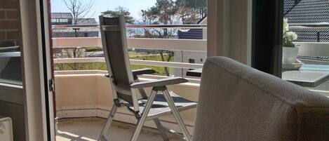 Un balcon avec une chaise et une table, donnant sur un parking et des immeubles.
