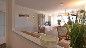A living room with a sofa, a television, a dining area with chairs, and a window with curtains. - Haus Belvedere App. 45 Wlan Inkl (Grömitz)