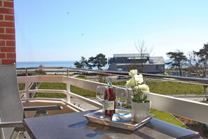 Un balcon avec une table, une bouteille de vin, deux verres et un vase rempli de fleurs.