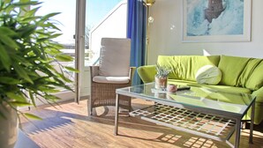 A modern living room with a glass coffee table, a green sofa, a wicker chair, and a potted plant. - Haus Belvedere App. 63 (Grömitz)