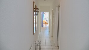 A narrow hallway with white tiled floors and walls, leading to a room with a table and chairs. - Haus Belvedere App. 64 (Grömitz)