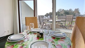 Une table à manger dressée avec des assiettes, des verres et des couverts, donnant sur un espace extérieur pittoresque.