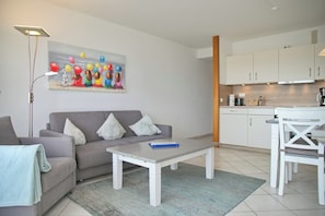 A modern living room with a grey sofa, white coffee table, and a painting on the wall.