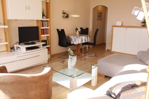 Un salon moderne avec une table basse en verre, un téléviseur à écran plat, un canapé et une table à manger avec des chaises.