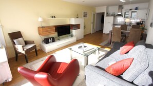 A modern living room with a sofa, red chairs, a glass coffee table, and a TV. - Haus Belvedere App. 75 Wlan Inkl (Grömitz)