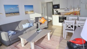 A modern living room with a grey sofa, a coffee table, and a kitchen area with white cabinets and a microwave. - Haus Belvedere App. 77 Wlan Inkl (Grömitz)