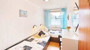 Une chambre avec deux lits, un bureau, une fenêtre avec des rideaux et un luminaire fixé au mur.