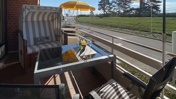 Un espace extérieur aménagé avec des sièges, protégé par un auvent, doté de coussins à rayures et de parasols jaunes, et offrant une vue sur une route.