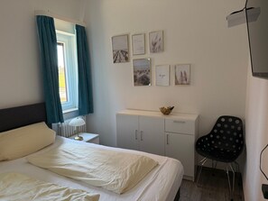 A hotel room with a bed, a desk, a chair, and wall art. - Haus Belvedere App. 19 Wlan Inkl (Grömitz)
