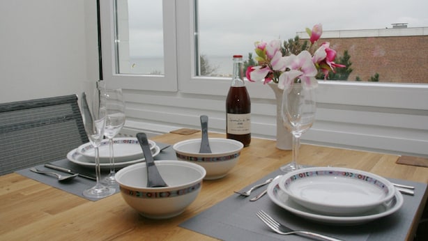 A dining table set with white plates, bowls, and cutlery, a bottle of wine, and a vase with flowers.