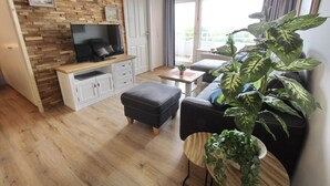 Un salon moderne avec un mur en bois, un téléviseur à écran plat, un canapé, un pouf, une table basse et une grande plante en pot.