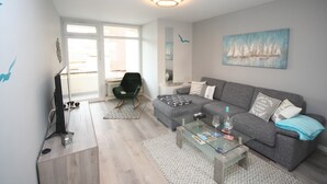 Un salon moderne avec un canapé gris, une table basse en verre et un téléviseur posé sur un meuble en bois.