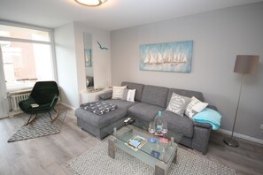 A modern living room with a grey sofa, a glass coffee table, and a green chair. - Villa am Meer App. 27 Inkl. Wlan (Grömitz)
