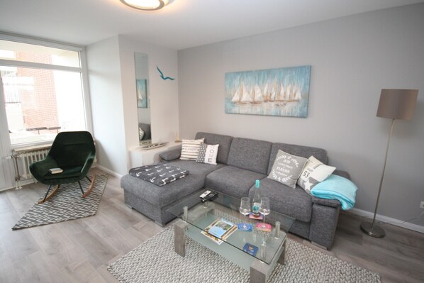 Una sala moderna con un sofá gris, una mesa de centro de vidrio y un sillón verde.