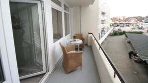 Un balcon avec une table et des chaises, un pot de fleurs et une vue sur la rue en contrebas.