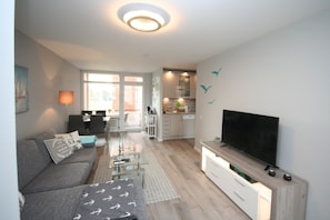 Una sala de estar moderna con un sofá gris, un televisor de pantalla plana y una zona de comedor con una mesa de vidrio.