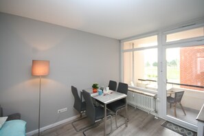 Een eetgedeelte met een tafel en stoelen, een vloerlamp en een uitzicht door een glazen deur op een buitengebied.