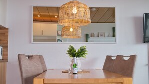 A dining area with a wooden table, two brown upholstered chairs, a wicker pendant light, and a small potted plant on the table. - Fürstenhof App. 430 mit Meerblick und Wlan (Grömitz)