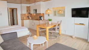 A modern apartment with a kitchenette, a dining area, a living room with a sofa, and a TV. - Fürstenhof App. 430 mit Meerblick und Wlan (Grömitz)