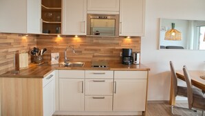 A modern kitchen with wooden cabinetry, a built-in oven, and a coffee maker. - Fürstenhof App. 430 mit Meerblick und Wlan (Grömitz)