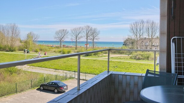 Een balkon met uitzicht op een strand, een geparkeerde auto en een grasveld met bomen.