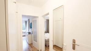 Een gang met een houten vloer, witte wanden en een deur met een spiegel.