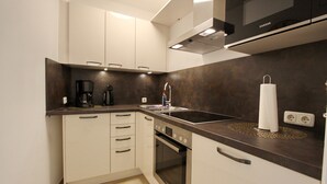 Une cuisine moderne avec des meubles blancs, un four encastré, une plaque de cuisson et une machine à café.