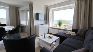 Un salon moderne avec un canapé, une table basse, un téléviseur et une vue sur la mer.