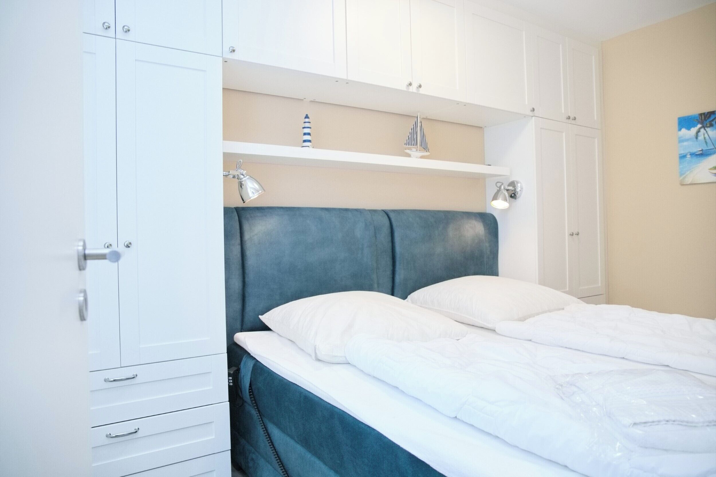A bedroom with a bed, white cabinets, and a shelf with decorative items.