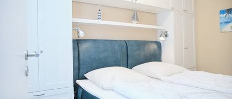A bedroom with a bed, white cabinets, and a shelf with decorative items.
