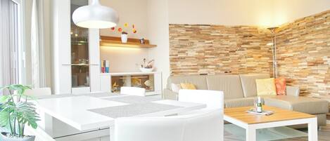 Ein modernes Wohnzimmer mit einem weißen Sofa, einem Couchtisch und einem Essbereich mit weißem Tisch und Stühlen.